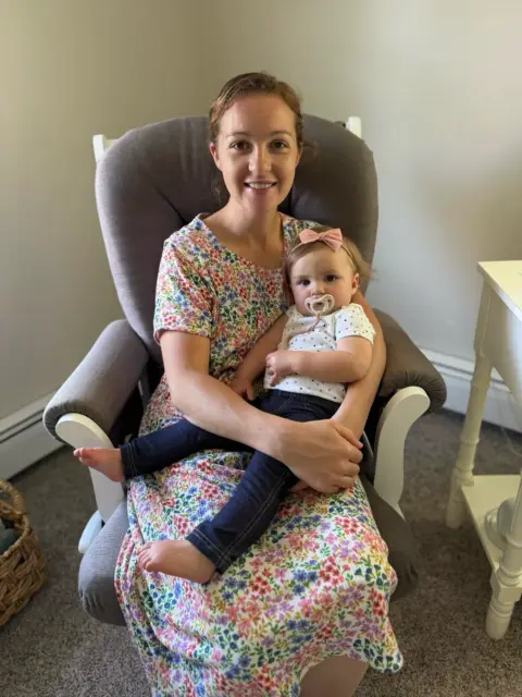 Charlotte's sitting, holding her baby, and enjoying rocking her baby to sleep.