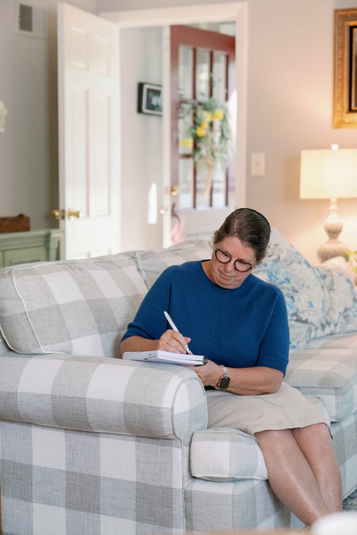 Middle-aged woman sitting on a couch in a living room writing in her weekly planner