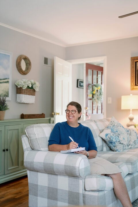 Smiling middle-aged woman sitting on a couch in a living room writing in her weekly planner