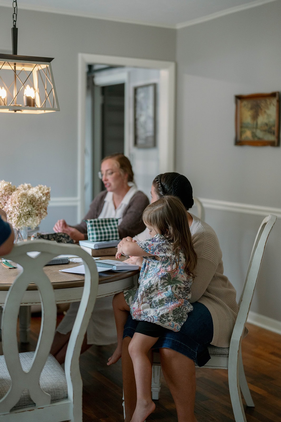 Women and a child sitting at a table having a discussion with weekly planners and purses on the table